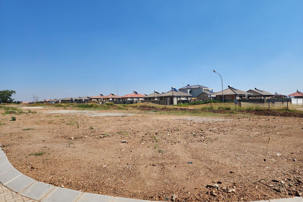 A view of a vacant residential plot with a paved curb in the foreground, situated in a developed neighborhood.
