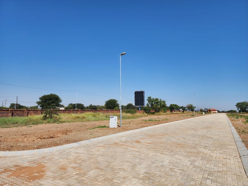 A view of a paved residential street with established boundary walls, street lighting, and utility infrastructure in a vacant land development.