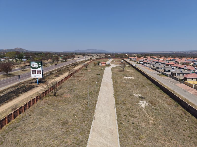 Aerial view of a vacant residential plot featuring a paved driveway, perimeter walling, and proximity to established residential developments and main road access.