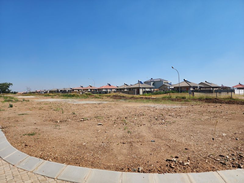 A view of a vacant residential plot with a paved curb in the foreground, situated in a developed neighborhood.