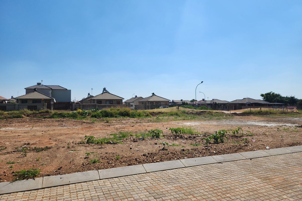 A vacant residential plot featuring a paved sidewalk and kerbing, situated in a developed neighborhood with surrounding residential properties.