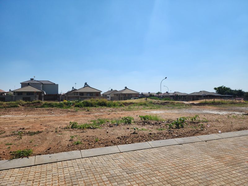 A vacant residential plot featuring a paved sidewalk and kerbing, situated in a developed neighborhood with surrounding residential properties.
