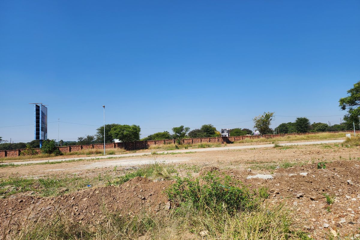 A vacant residential plot featuring a perimeter brick wall and clear street access, suitable for future development.