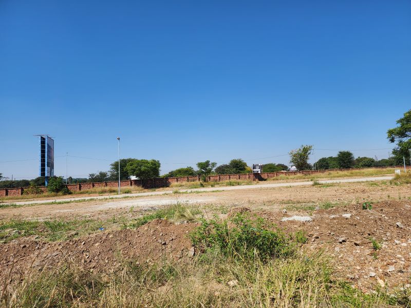 A vacant residential plot featuring a perimeter brick wall and clear street access, suitable for future development.