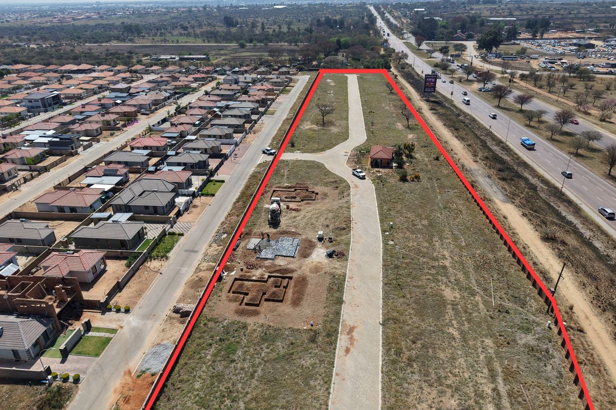 Aerial view of a residential development site showing paved access, a small existing structure, and ongoing foundation excavations for new construction.