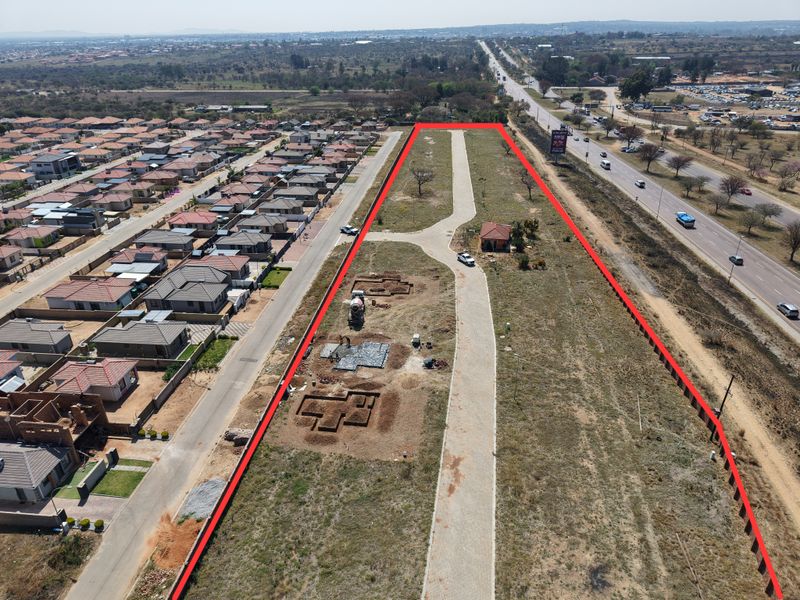 Aerial view of a residential development site showing paved access, a small existing structure, and ongoing foundation excavations for new construction.