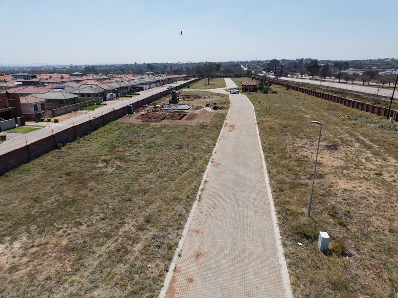 Aerial view of a vacant residential land plot featuring a paved driveway, perimeter walling, and ongoing foundation work.