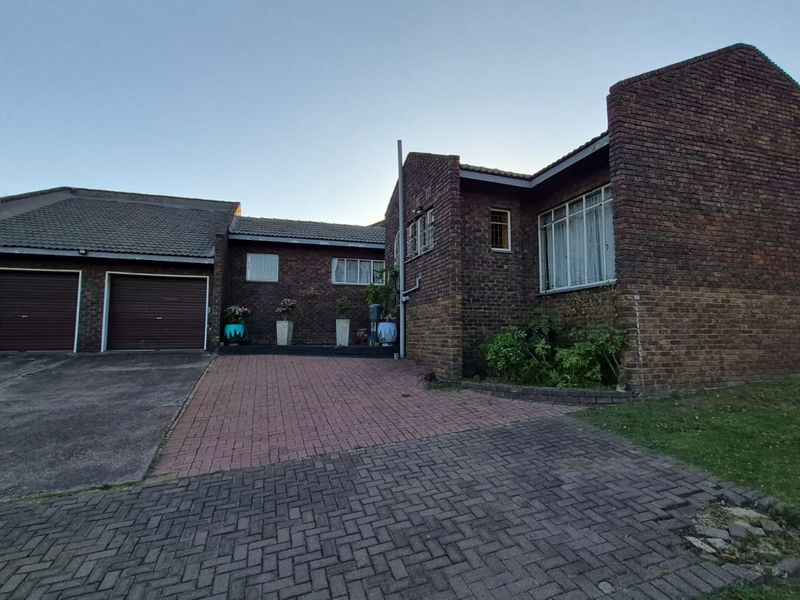 Front elevation of a face-brick house featuring a double garage, paved driveway, and established garden area.