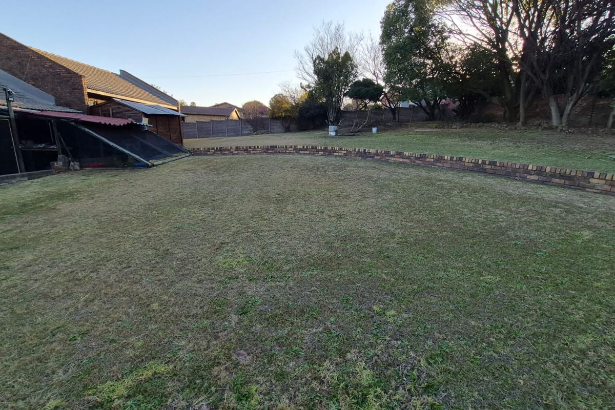 A spacious rear garden featuring a large lawn area, a low brick retaining wall, and established trees along the perimeter.