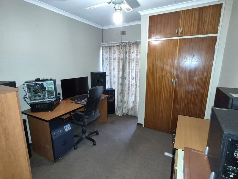A bedroom featuring built-in wooden cupboards, a ceiling fan, and carpeted flooring, currently utilized as a home office space.