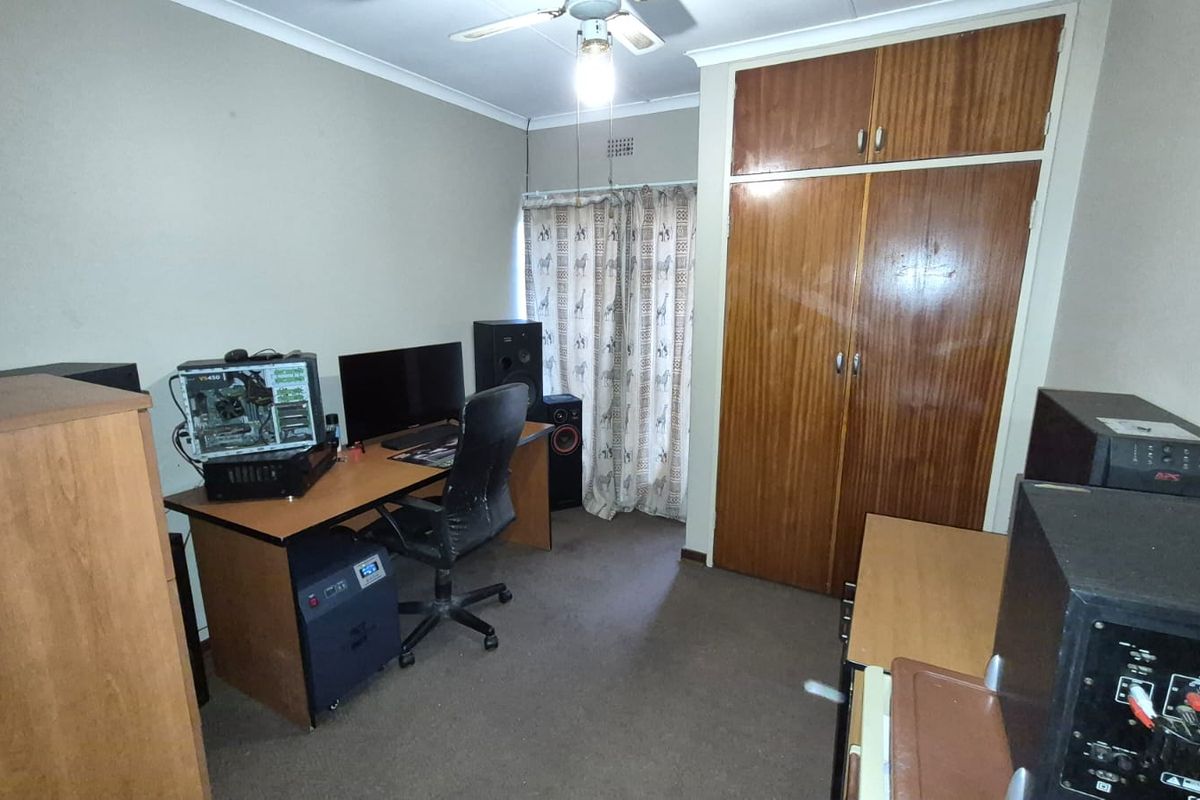 A bedroom featuring built-in wooden cupboards, a ceiling fan, and carpeted flooring, currently utilized as a home office space.