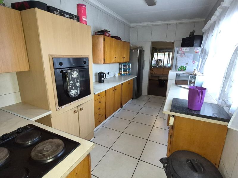 A functional kitchen featuring built-in cabinetry, an integrated oven, electric hob, and tiled surfaces throughout, offering potential for modernization.