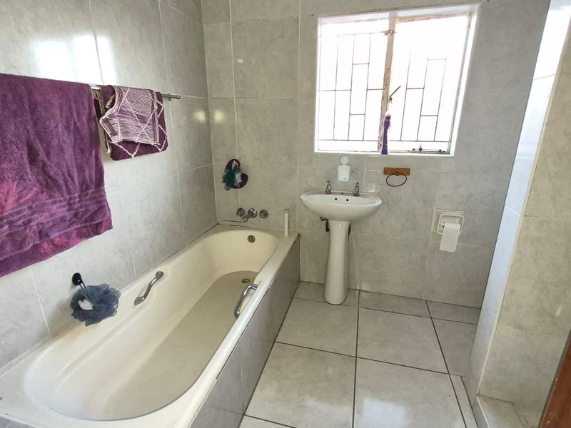 A functional bathroom featuring a pedestal washbasin, a built-in bathtub, and neutral ceramic tiling throughout.