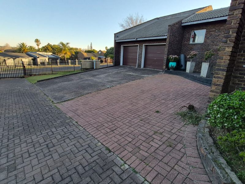 Front exterior view of the property featuring a double garage, brick facade, and a paved driveway with perimeter metal fencing.