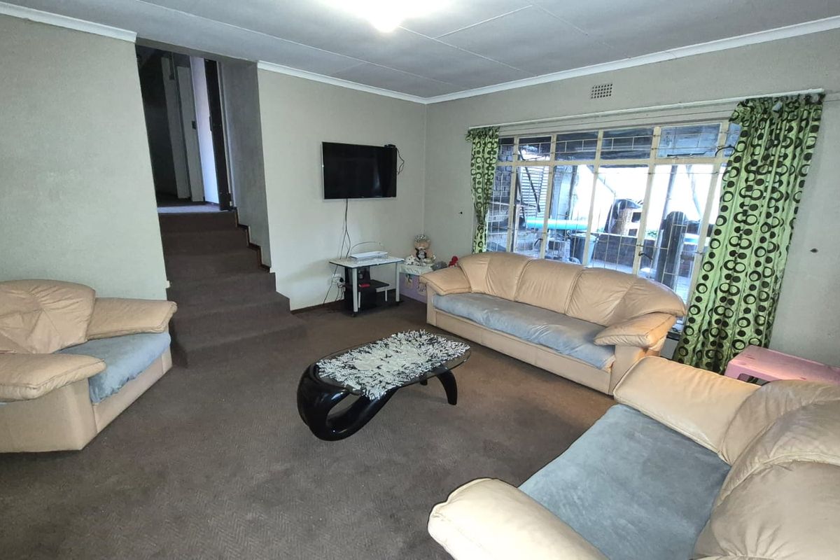 A spacious living room featuring carpeted flooring, a large window with natural light, and an internal staircase leading to another level.