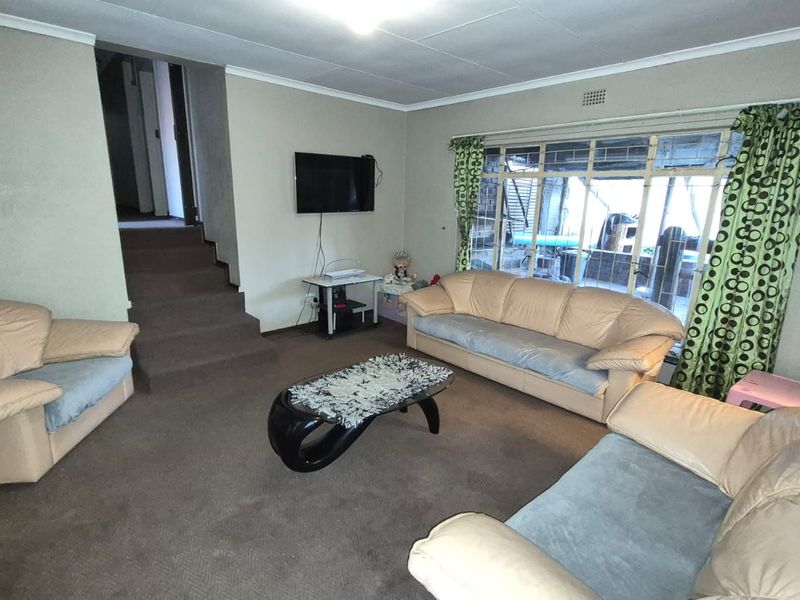 A spacious living room featuring carpeted flooring, a large window with natural light, and an internal staircase leading to another level.