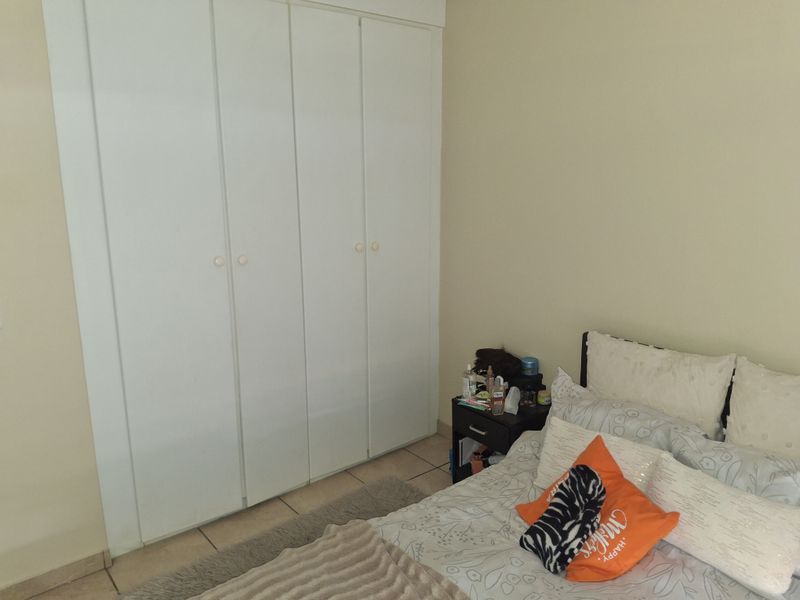 A bedroom featuring tiled flooring and a large white built-in wardrobe with multiple doors.