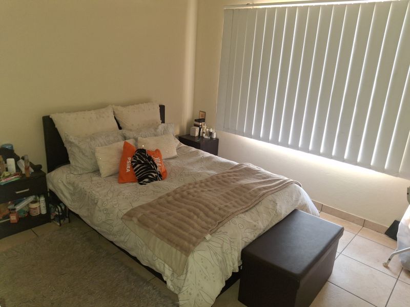 A bedroom featuring tiled flooring and vertical window blinds, providing a functional space with neutral wall finishes.