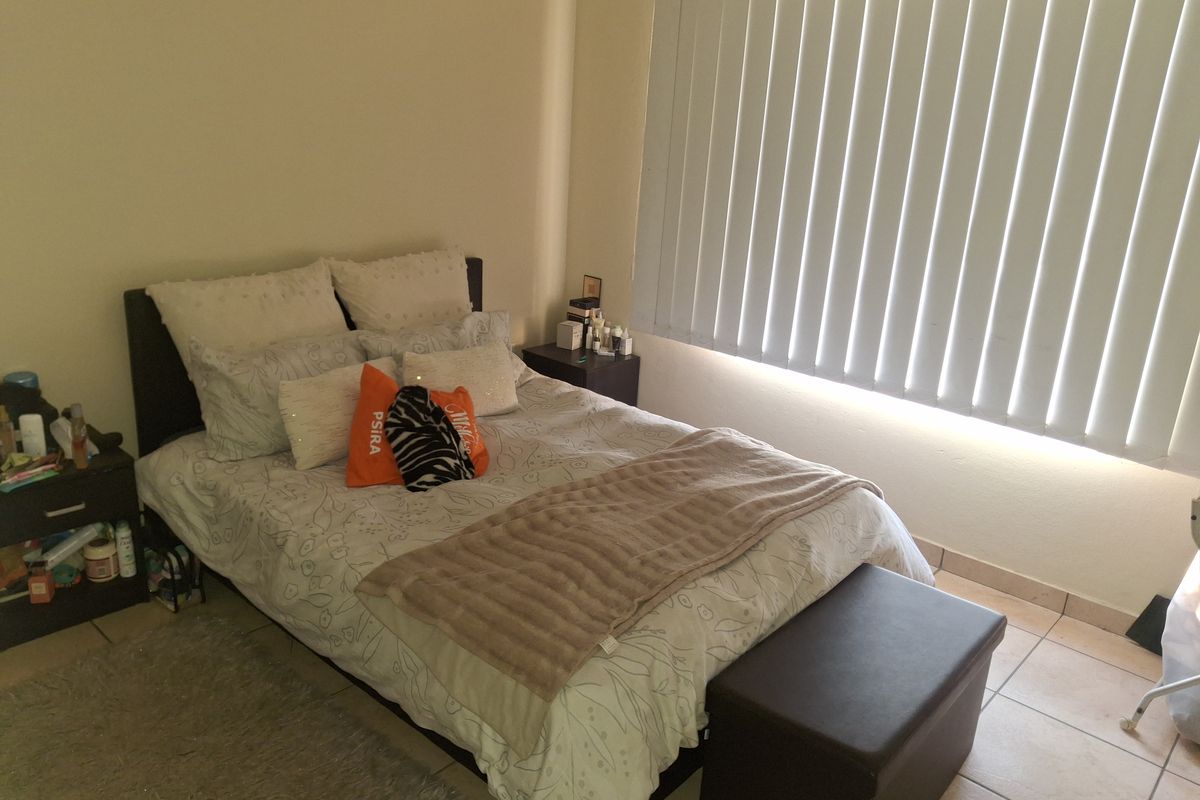 A bedroom featuring tiled flooring and vertical window blinds, providing a functional space with neutral wall finishes.
