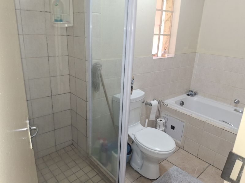 A functional bathroom featuring a shower enclosure, a built-in bathtub, and a toilet, with tiled finishes throughout.