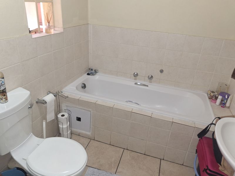 A functional bathroom featuring a built-in bathtub, tiled walls and flooring, a standard toilet, and a basin with chrome fixtures.