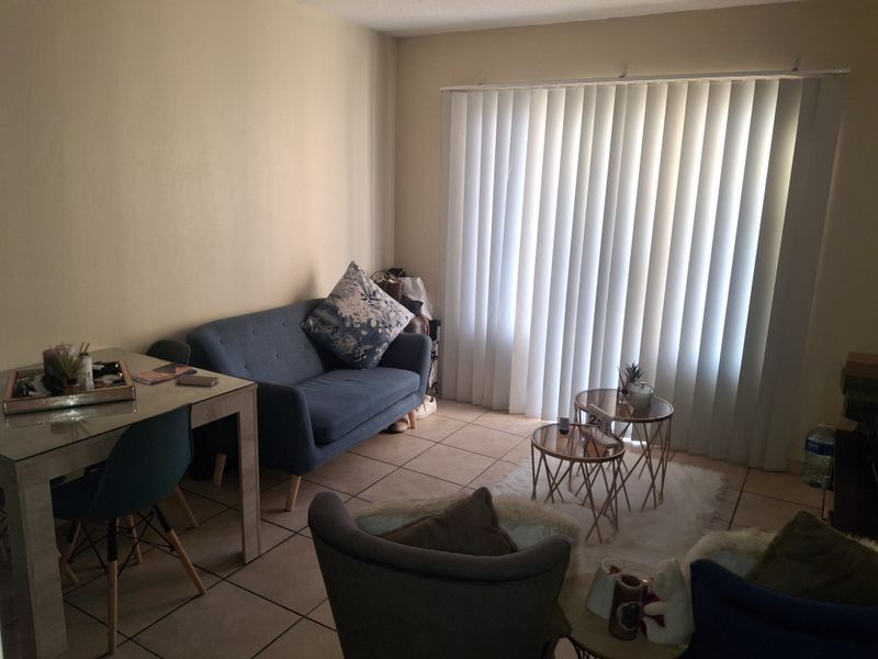 A living room area featuring tiled flooring and vertical blinds covering a sliding door, providing natural light to the space.