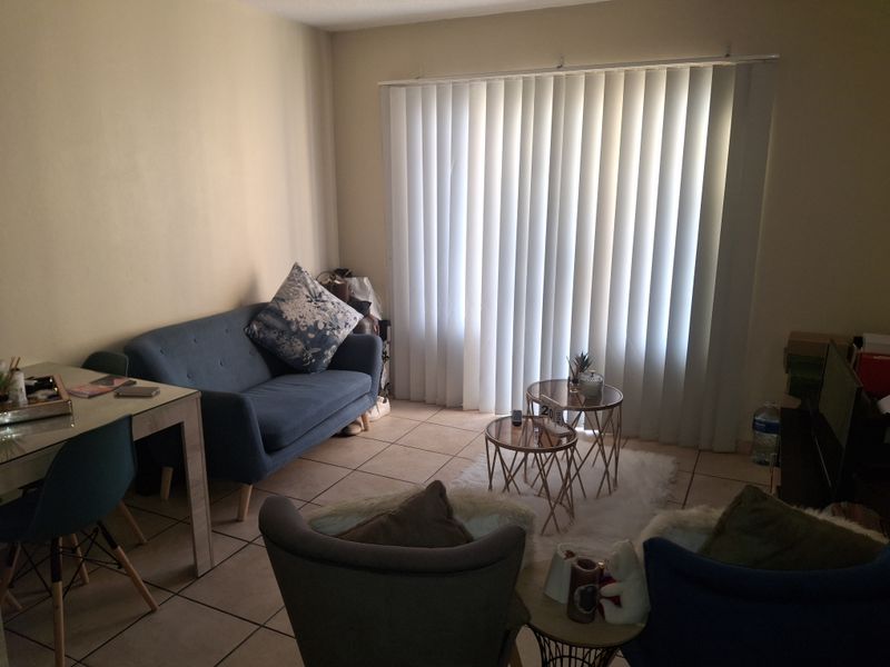 A living room area featuring tiled flooring and vertical blinds covering a large window, providing a functional and neutral space.