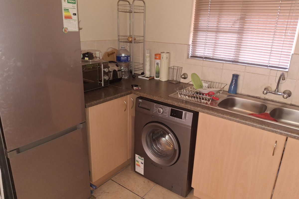 Compact kitchen featuring laminate cabinetry, double bowl stainless steel sink, tiled backsplash, and tiled flooring with integrated appliance space.