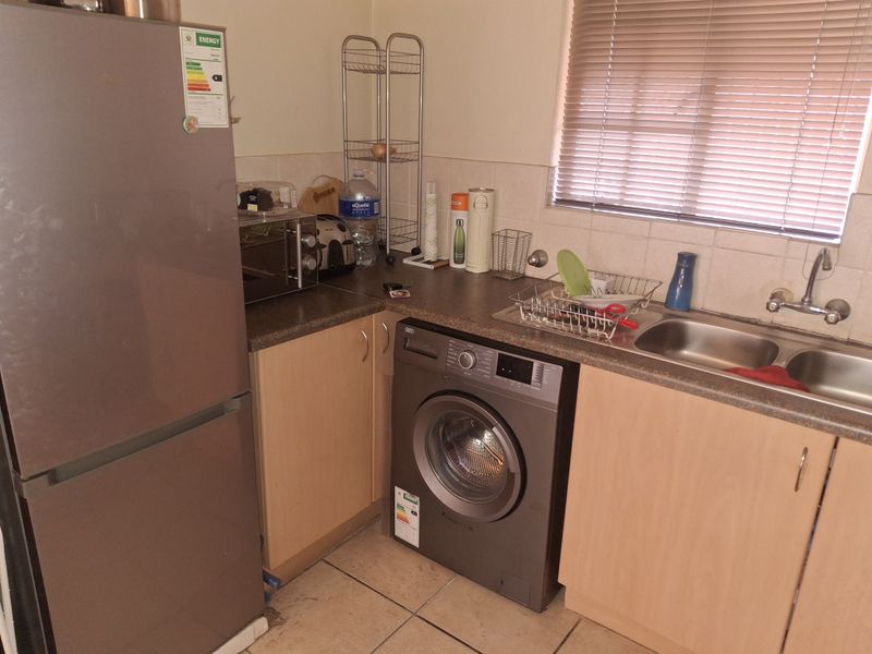 Compact kitchen featuring laminate cabinetry, double bowl stainless steel sink, tiled backsplash, and tiled flooring with integrated appliance space.