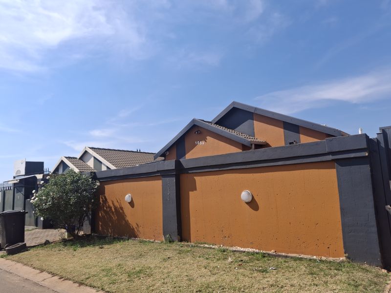 Front view of the property featuring a perimeter wall, tiled roof, and paved driveway access.