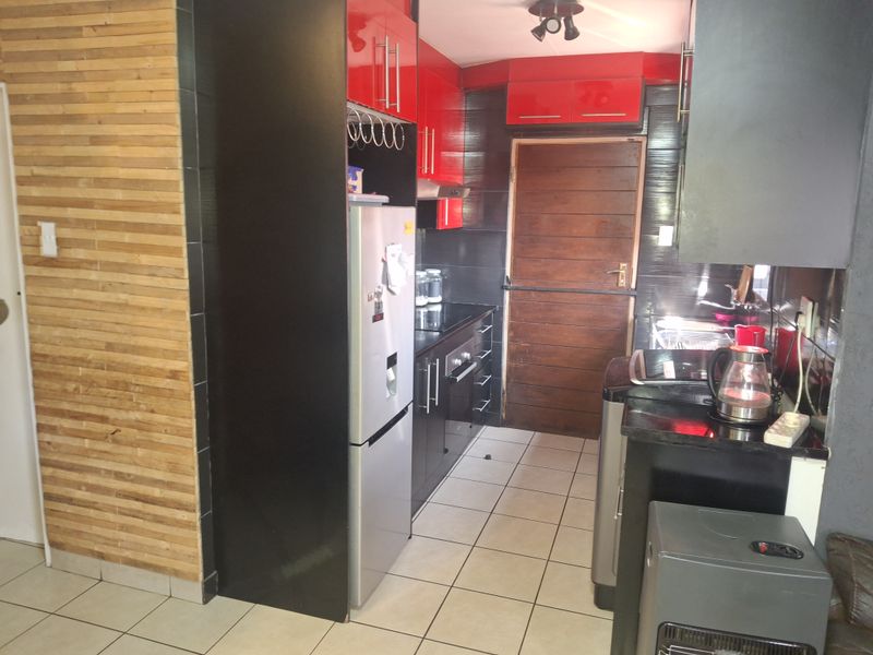 Compact kitchen featuring high-contrast red and black cabinetry, black granite countertops, built-in oven, extractor fan, and decorative timber wall paneling.