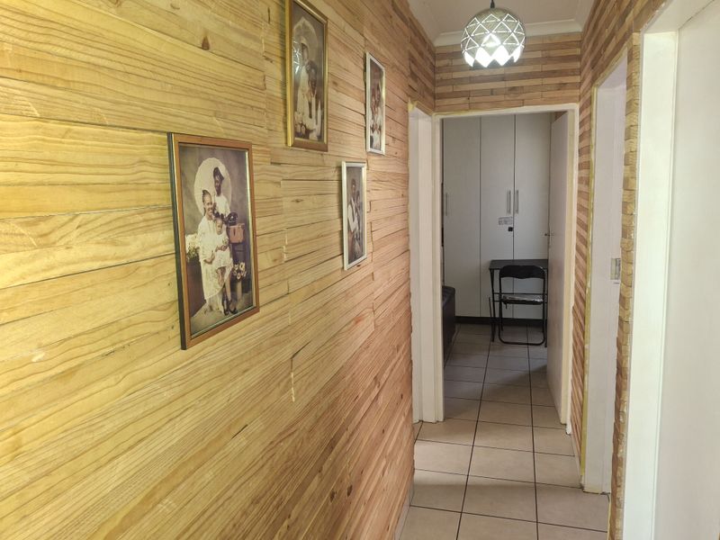 A hallway featuring timber wall cladding, tiled flooring, and access to a bedroom with built-in cupboards.