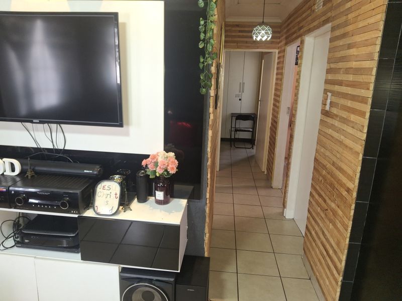 Living area featuring a modern built-in media console, decorative timber slat wall paneling, and neutral ceramic floor tiles leading into a hallway.