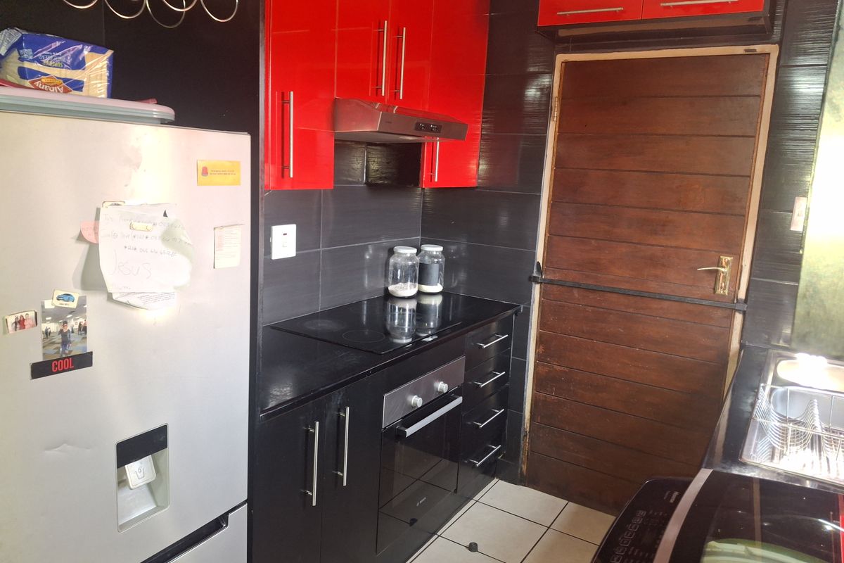 A compact kitchen featuring high-contrast red and black cabinetry, a built-in oven and hob, and tiled finishes.