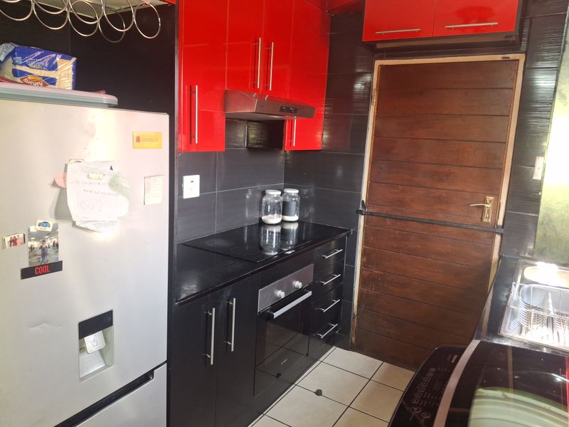 A compact kitchen featuring high-contrast red and black cabinetry, a built-in oven and hob, and tiled finishes.