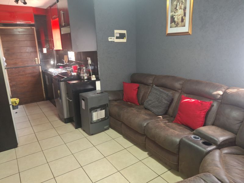 Open plan living area featuring tiled flooring and a compact kitchen with built-in cabinetry and dark finishes.