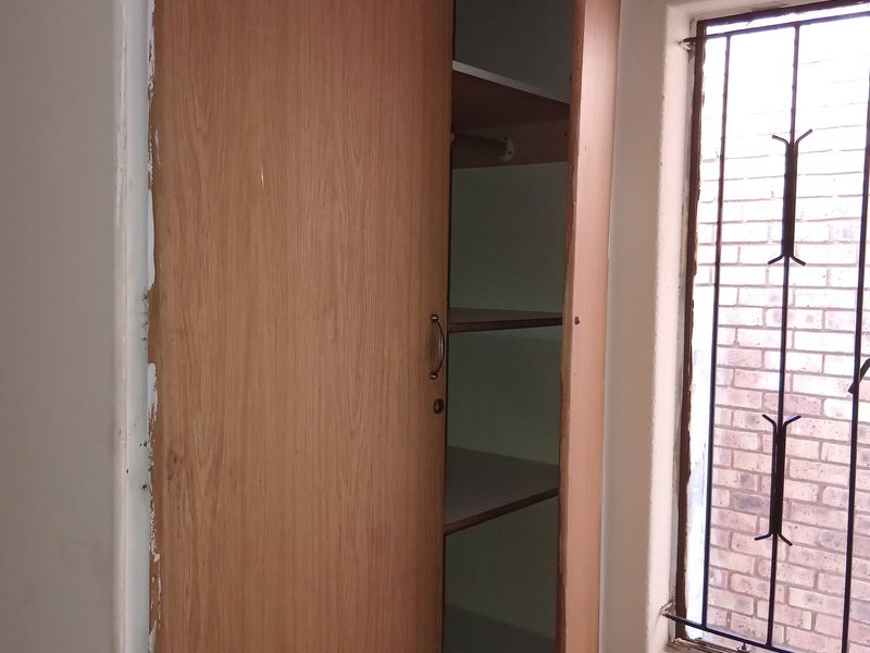 A bedroom featuring a built-in wooden cupboard and a window fitted with security bars.