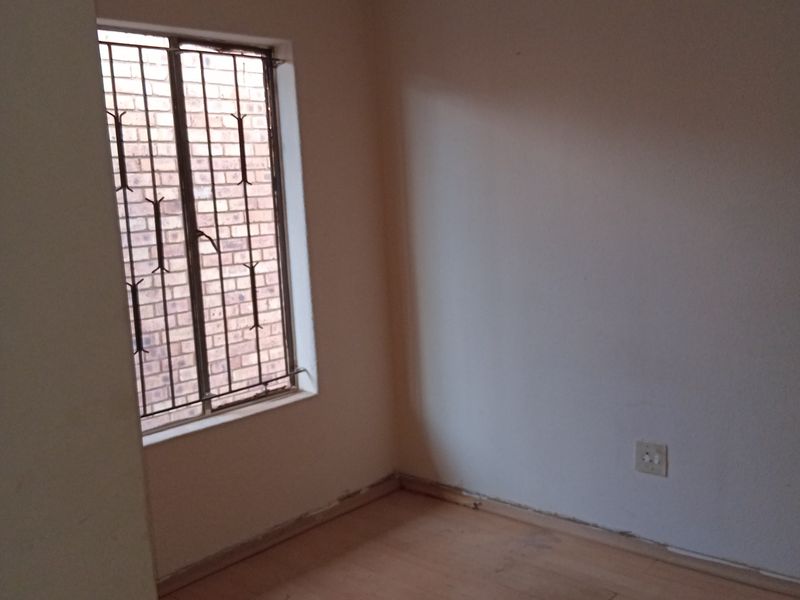 An empty bedroom featuring tiled flooring, a window with security bars, and plain walls, requiring minor cosmetic updates to skirting and flooring.
