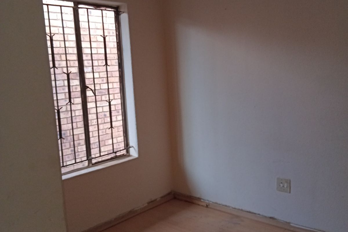 An empty bedroom featuring tiled flooring, a window with security bars, and plain walls, requiring minor cosmetic updates to skirting and flooring.