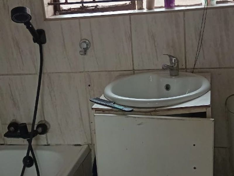 A compact bathroom featuring a bathtub, a wall-mounted shower head, and a vanity cabinet with a washbasin, finished with tiled walls and flooring.