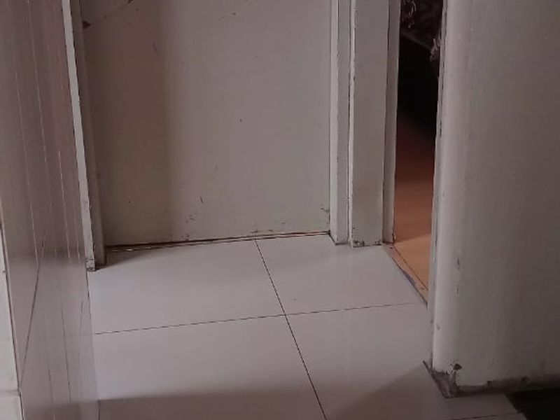 A narrow hallway featuring tiled flooring and internal doors, showing signs of wear on the door frames and paintwork.