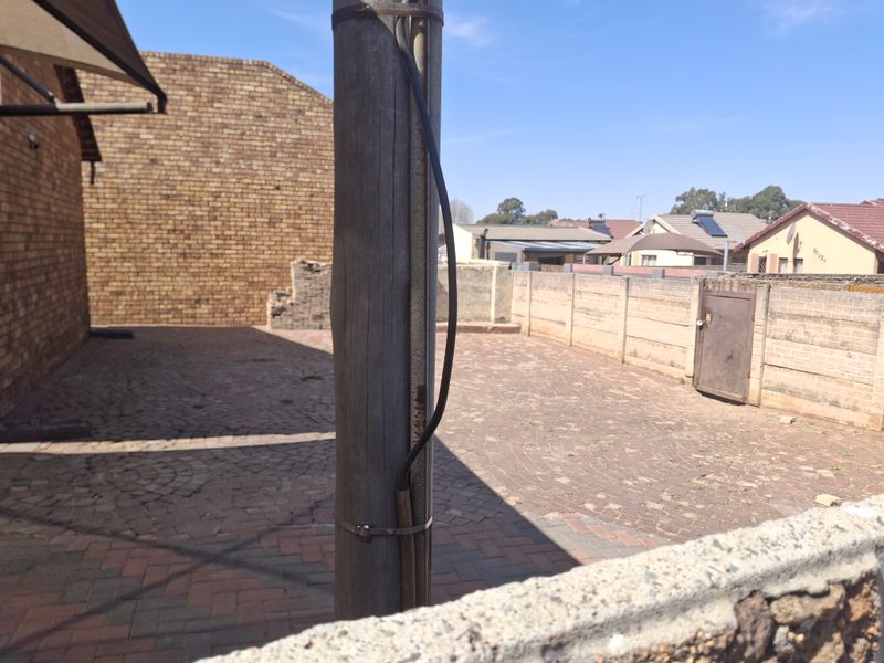 A paved rear courtyard area enclosed by brick boundary walls, featuring a metal access gate and a central wooden utility pole.