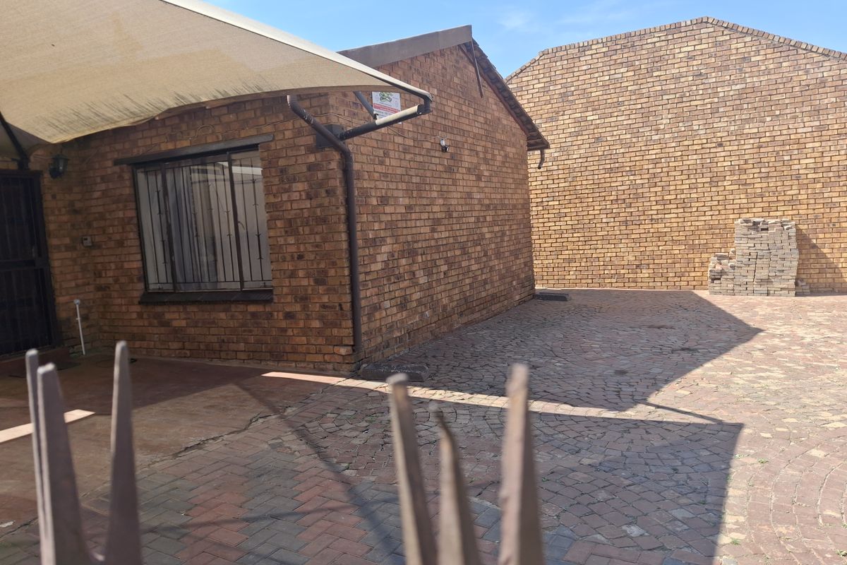 Rear exterior view of a face brick house featuring a paved courtyard area, shade sail, and security bars on the windows.