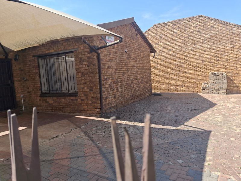 Rear exterior view of a face brick house featuring a paved courtyard area, shade sail, and security bars on the windows.