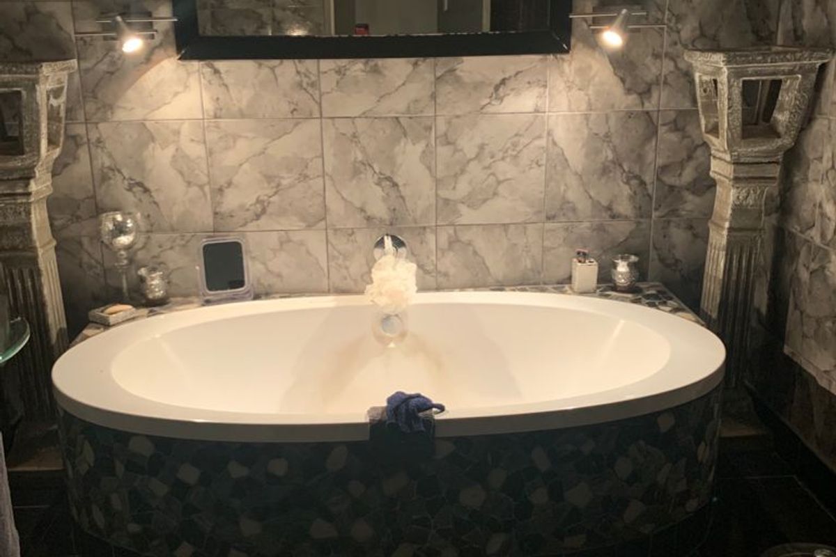 A bathroom featuring a central oval bathtub with wall-mounted faucet, surrounded by marble-effect wall tiling and dark floor tiles.