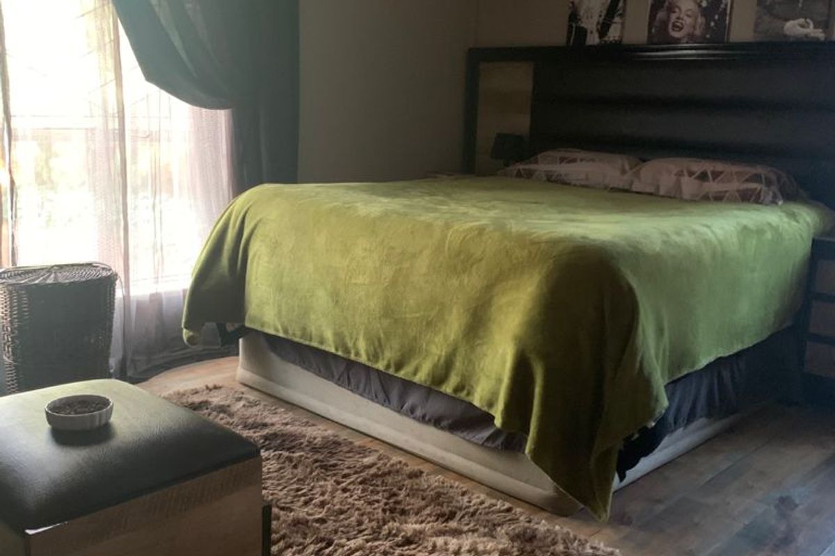 A bedroom featuring laminate flooring and a wall-mounted split-system air conditioner.
