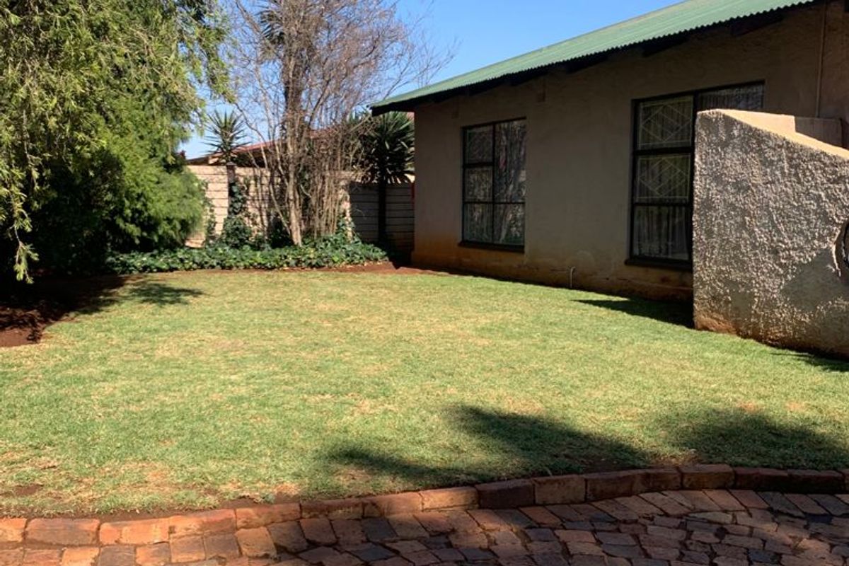 A rear garden view featuring a lawn, brick paved area, and the rear elevation of the house with a corrugated metal roof.