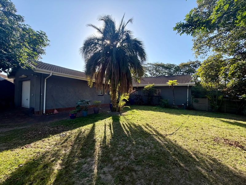 A view of the rear exterior of the house featuring a tiled roof, gutters, and a spacious lawn area with mature landscaping.