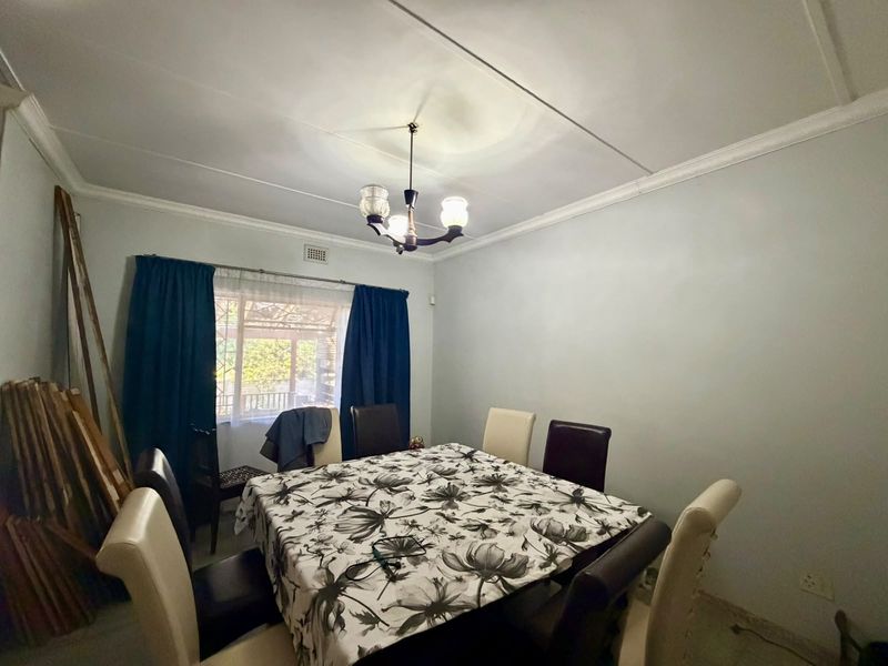 A dining room featuring a central light fixture, ceiling cornice, and a window overlooking the exterior area.