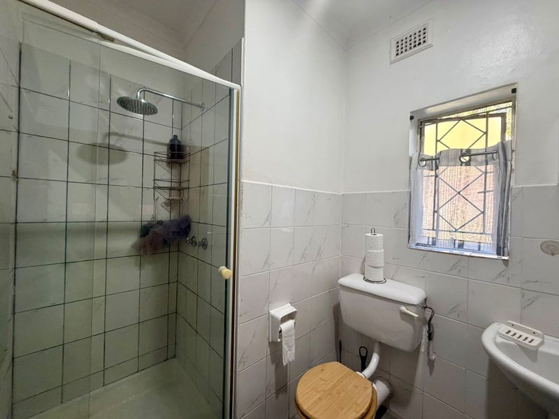 A functional bathroom featuring a glass-enclosed shower with a rainfall shower head, a standard toilet, and a wall-mounted basin with tiled walls.
